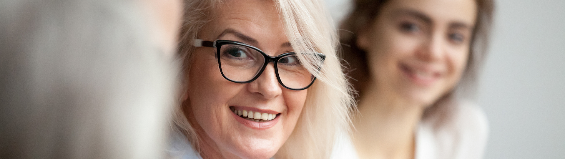 A woman with grey hair and glasses smiles.