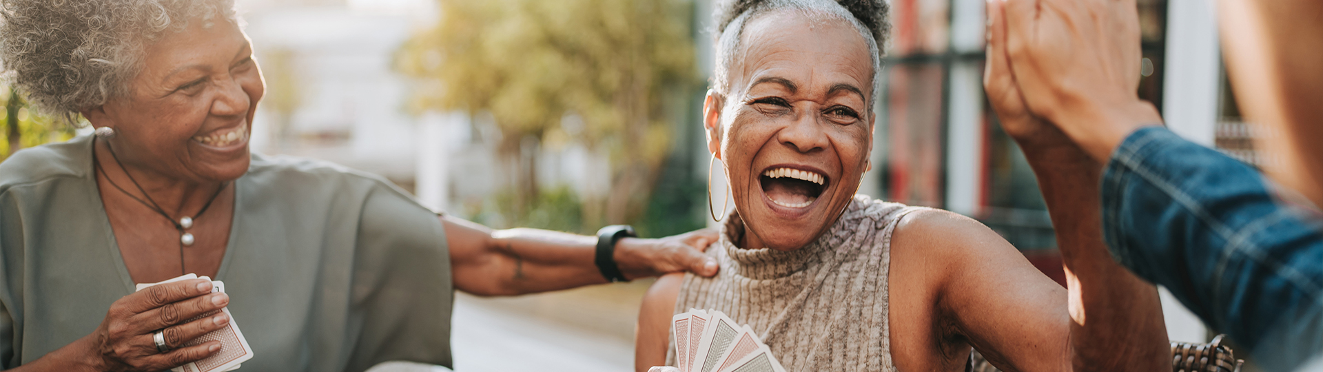 Two senior women play cards at a table and smile at each other.